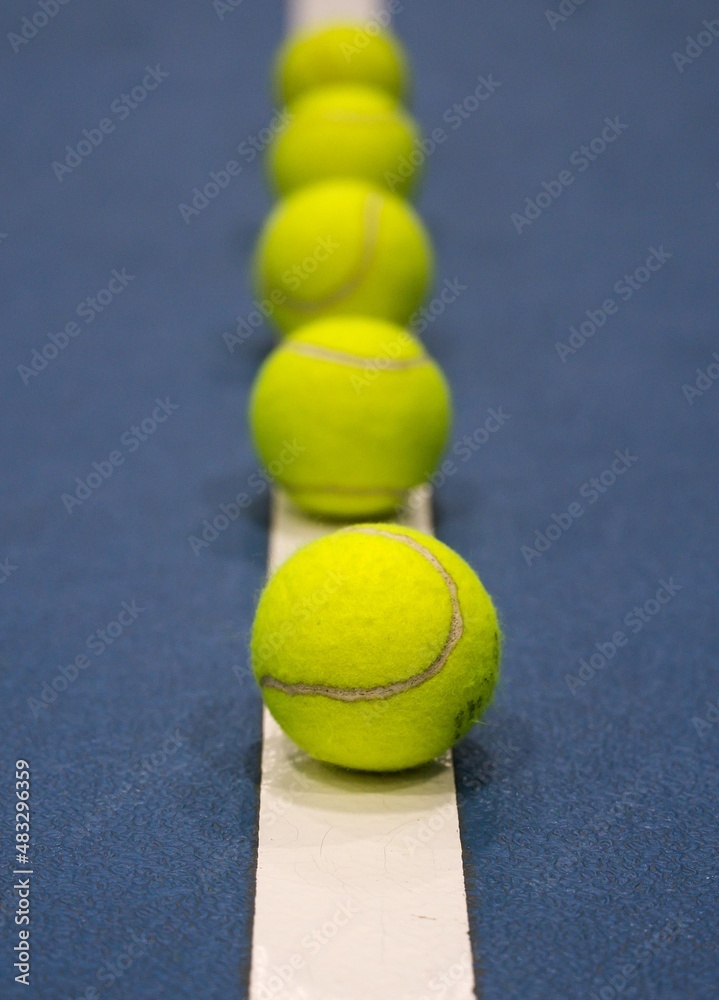 Row of tennis balls on white line on blue hard tennis court.