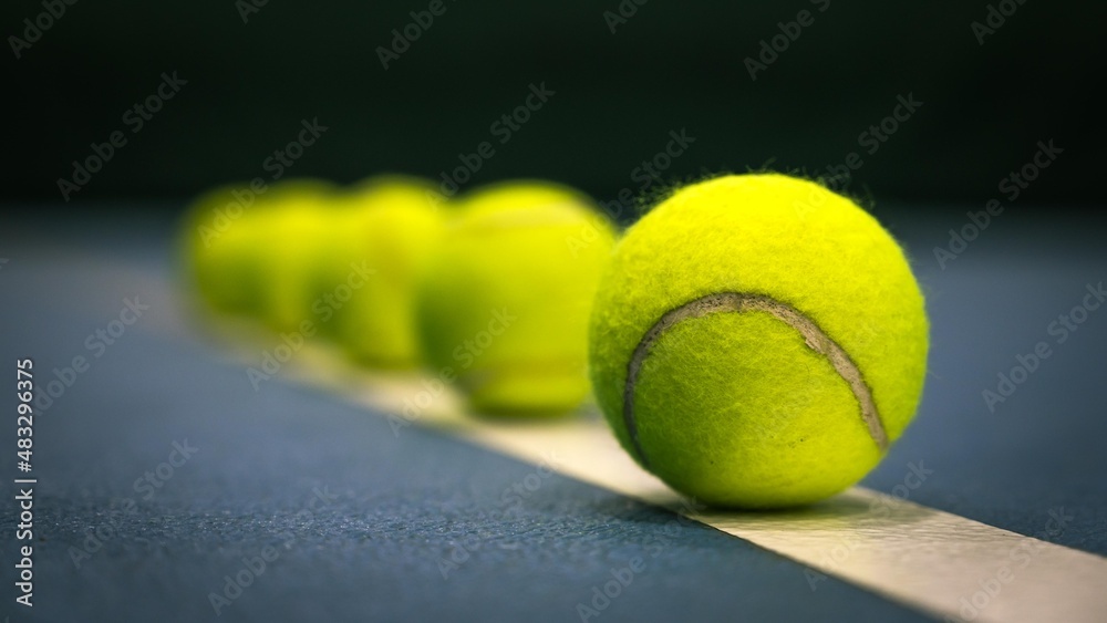 Row of tennis balls on white line on blue hard tennis court.