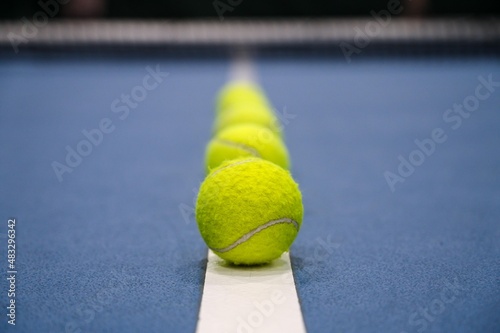 Row of tennis balls on white line on blue hard tennis court. © Anastasia