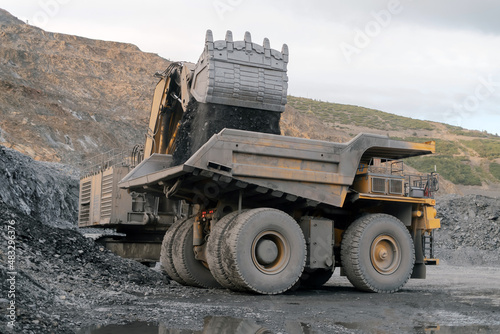 A heavy excavator loads ore into a dump truck. Gold mining site.