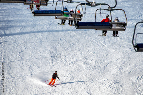 People sitting on chairlift and skiers skiing downhill on slope at mountain resort. photo