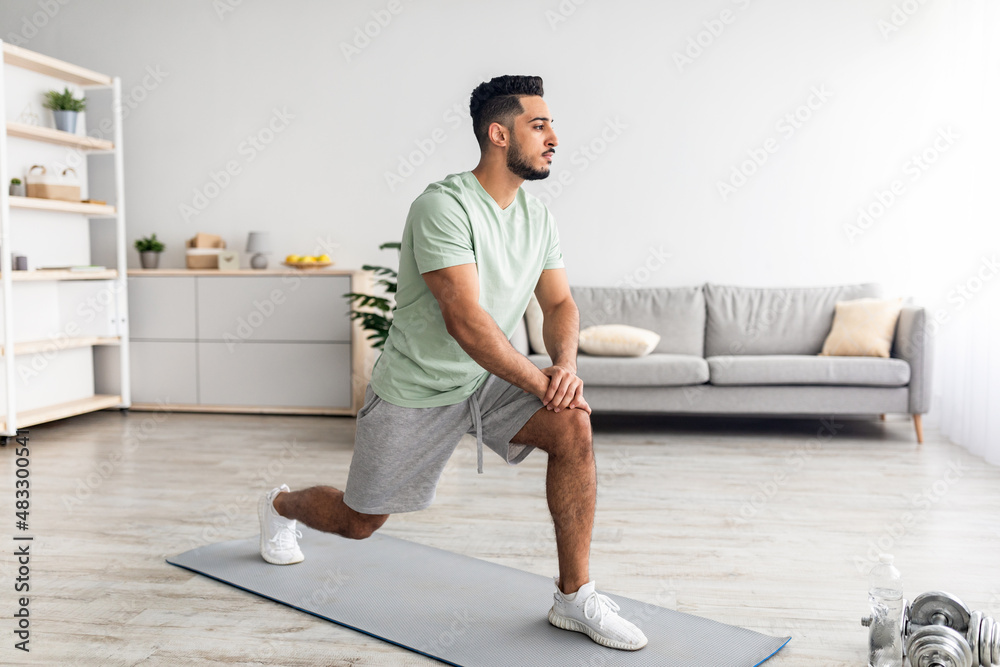 Fit young Arab guy making lunge, doing strength exercises, working out legs muscles at home, full length Fit young Arab guy making lunge, doing strength exercises, working out legs muscles at home, full length