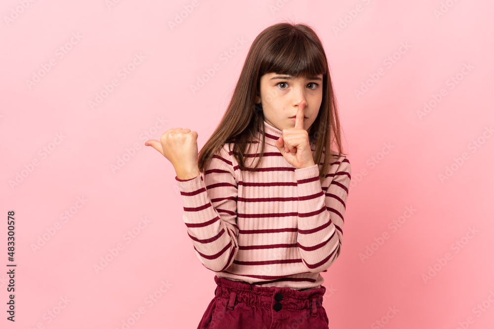 Little girl isolated on pink background pointing to the side and doing silence gesture Little girl isolated on pink background pointing to the side and doing silence gesture