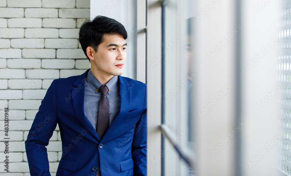 Portrait studio shot Asian handsome professional successful male businessman entrepreneur in formal blue suit necktie standing smiling look at camera on white brick wall background near office window