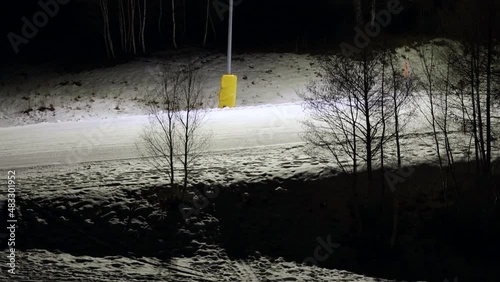 Night ski in the ski area of Aprica, in the Italian alps. A skier in fluo suit speeding downhill in aerodynamic position passing in front of camera.  photo