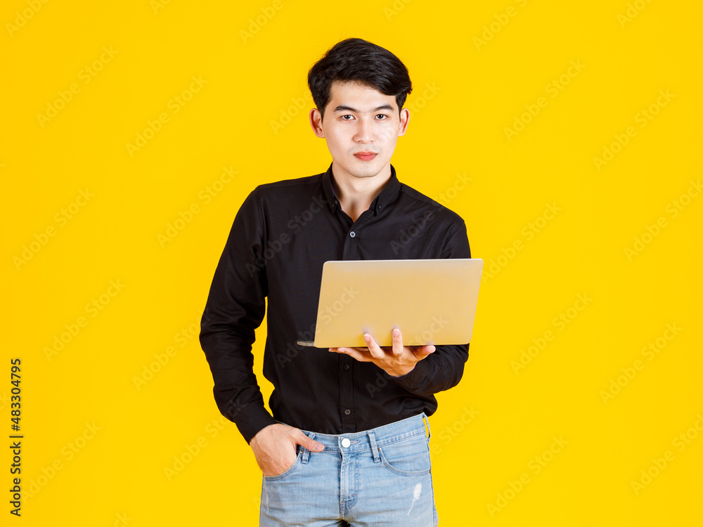 Portrait closeup studio shot of Asian man happy male businessman model in casual outfit standing holding laptop computer for advertising on yellow background Portrait closeup studio shot of Asian man happy male businessman model in casual outfit standing holding laptop computer for advertising on yellow background