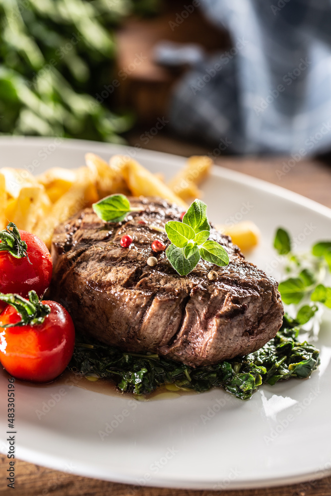 Medium rare sirloin steak on a plate served with spinach, tomatoes and fries Medium rare sirloin steak on a plate served with spinach, tomatoes and fries