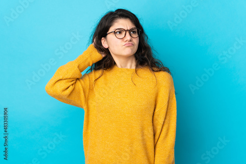 Teenager Russian girl isolated on blue background having doubts