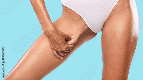 Unrecognizable young woman pinching her inner thigh, examining cellulite photo