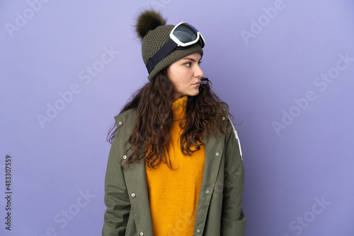 Teenager Russian girl with snowboarding glasses isolated on purple background looking to the side © luismolinero