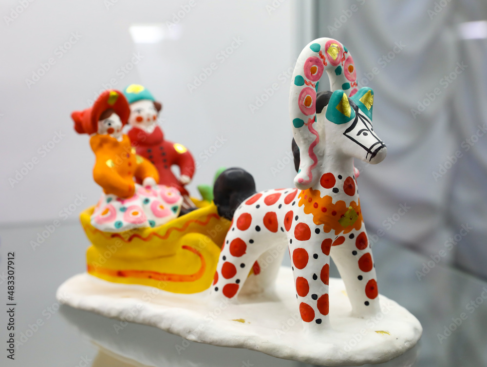 Horse and sled with pair of man and woman in dymkovo painting style with circles. Handicraft toy made by Russian craftsmen in the national traditions of Russia. Dymkovskaya clay toy. Selective focus