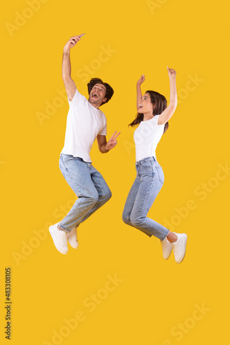 Excited millennial couple taking selfie and jumping at studio