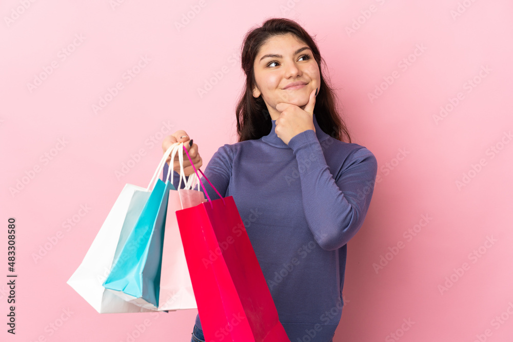 Teenager Russian girl isolated on pink background holding shopping bags and thinking