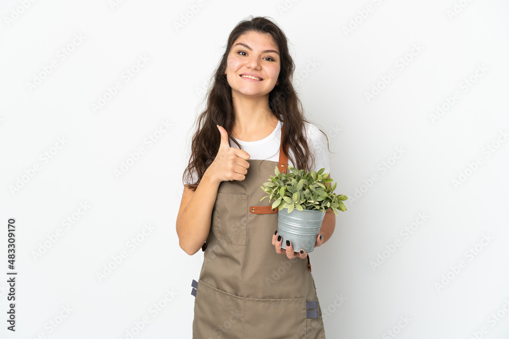 Young Russian gardener girl holding a plant isolated giving a thumbs up gesture Young Russian gardener girl holding a plant isolated giving a thumbs up gesture