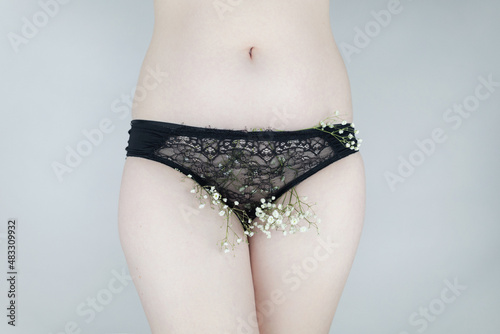 A woman has small flowers sticking out from under her underpants, imitating extra hair. Laser hair removal and shaving with a razor. Conceptual shot about women issues. Proper self care.