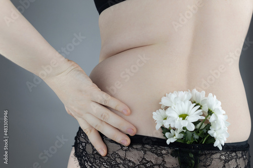 Close-up girl from behind. Side pleats. Excess weight. Adoption non-ideal figure. Body positivity among women. Concept shot. Flowers protrude from underpants, symbolizing acceptance one’s appearance.