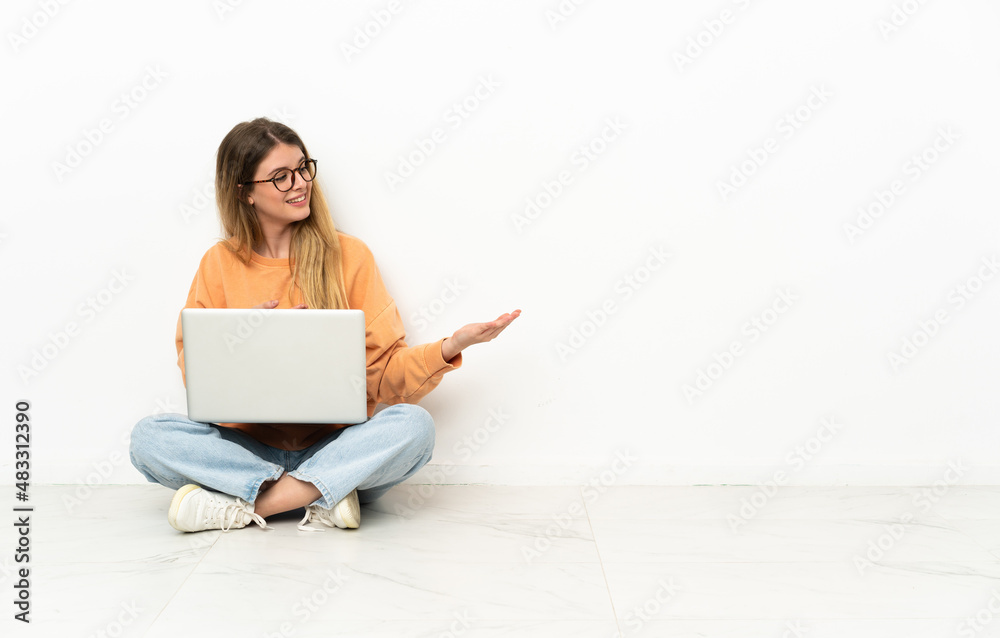 Young woman with a laptop sitting on the floor extending hands to the side for inviting to come Young woman with a laptop sitting on the floor extending hands to the side for inviting to come