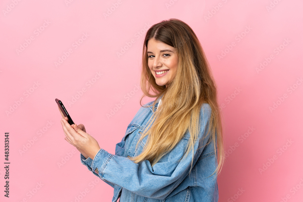 Young blonde woman isolated on blue background sending a message or email with the mobile Young blonde woman isolated on blue background sending a message or email with the mobile