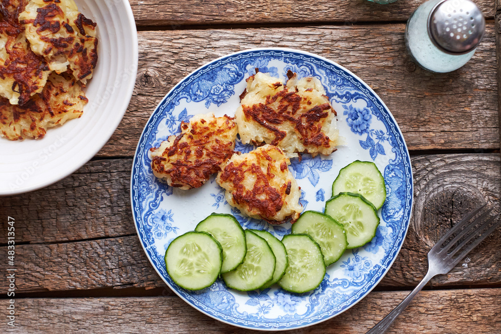Draniki and cucumbers on a blue plate. Top view, wooden background Draniki and cucumbers on a blue plate. Top view, wooden background