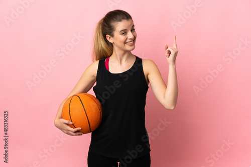 Young blonde woman playing basketball isolated on pink background showing and lifting a finger in sign of the best
