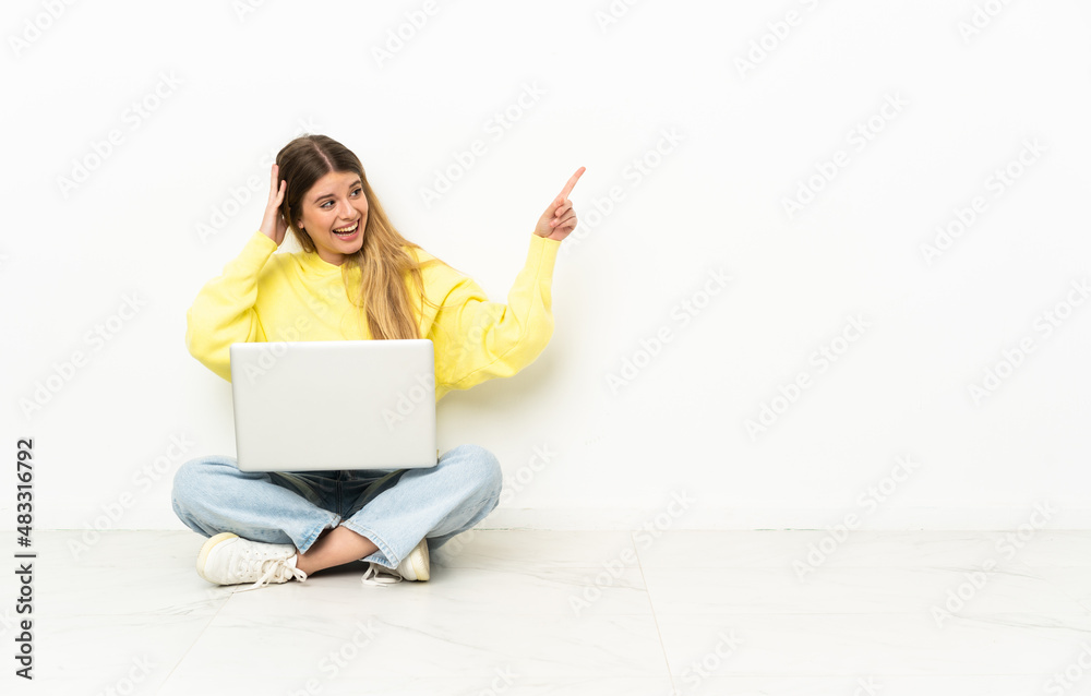Young woman with a laptop sitting on the floor surprised and pointing finger to the side Young woman with a laptop sitting on the floor surprised and pointing finger to the side