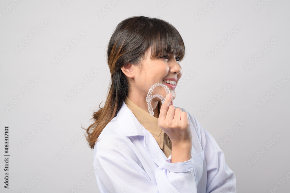 Young female dentist holding invisalign braces over white background studio, dental healthcare and Orthodontic concept. Young female dentist holding invisalign braces over white background studio, dental healthcare and Orthodontic concept.