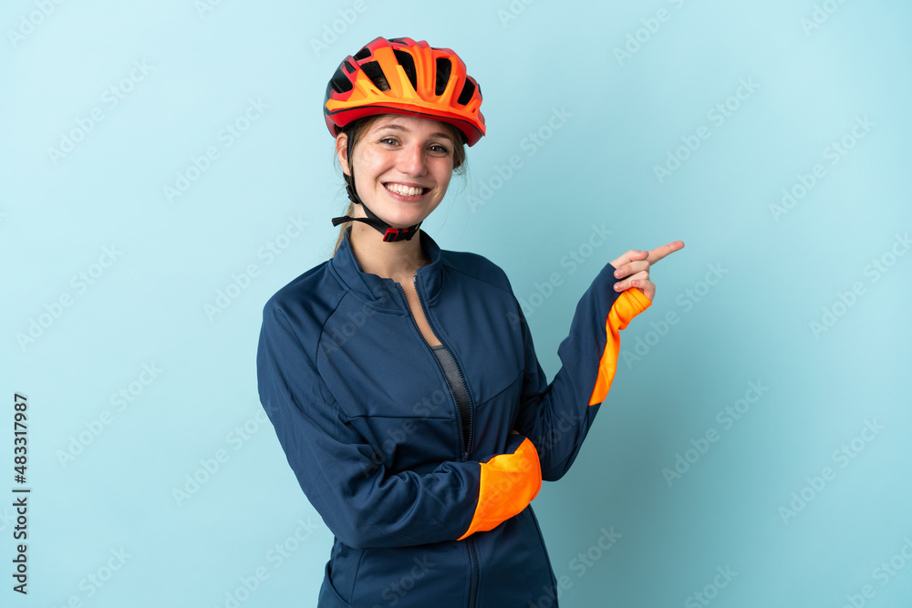Young cyclist woman isolated on blue background pointing finger to the side - obrazy, fototapety, plakaty 