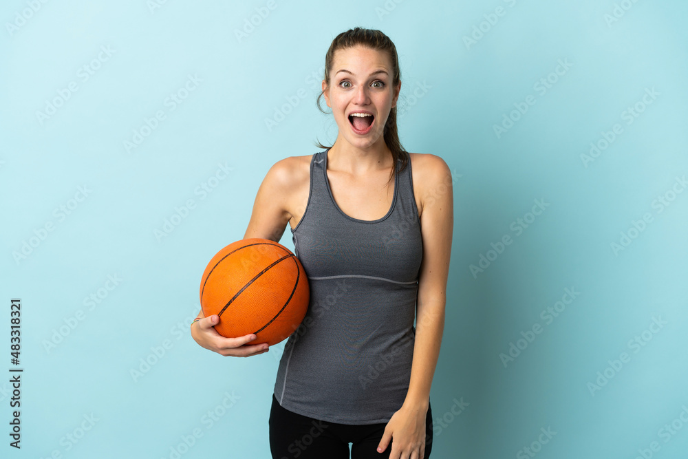 Young woman playing basketball isolated on blue background with surprise facial expression