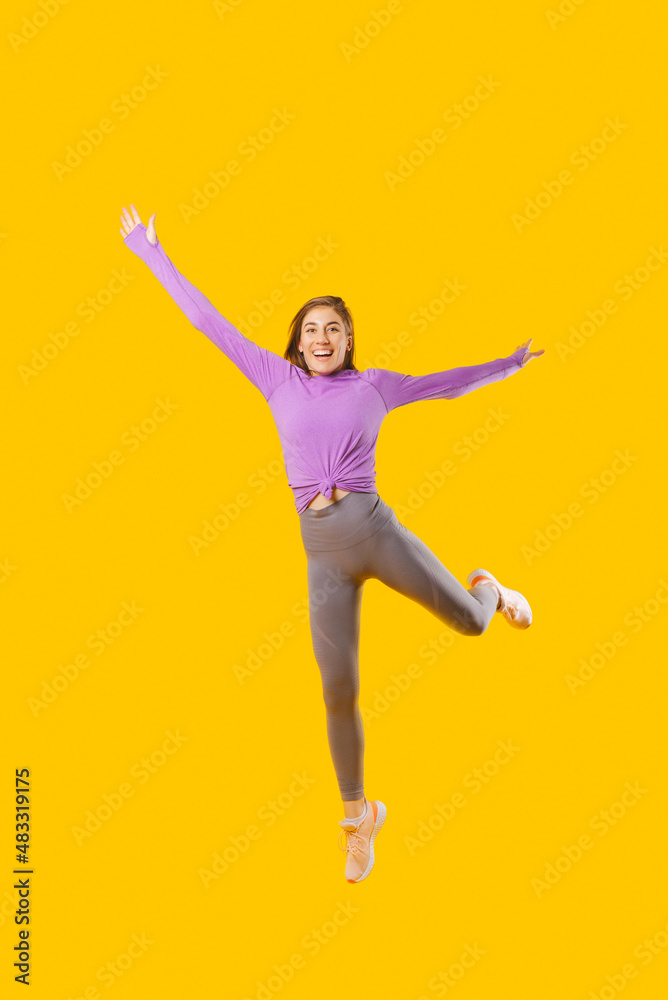 Photo of young joyful sport woman jumping over yellow background.