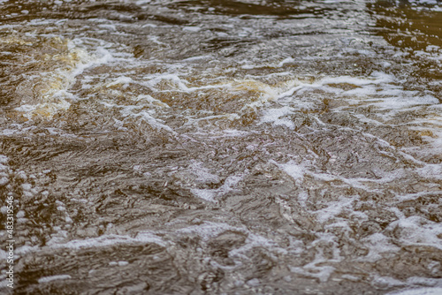 Waters of a river, turbulent that flow quickly, make waves and cause foam, the focus is in the center with the rest and the background blurred