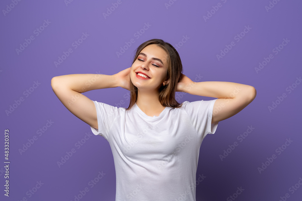 Portrait of dreaming brunette girl in blank white t shirt holding hands behind the had, close eyes and relax isolated on purple background Portrait of dreaming brunette girl in blank white t shirt holding hands behind the had, close eyes and relax isolated on purple background