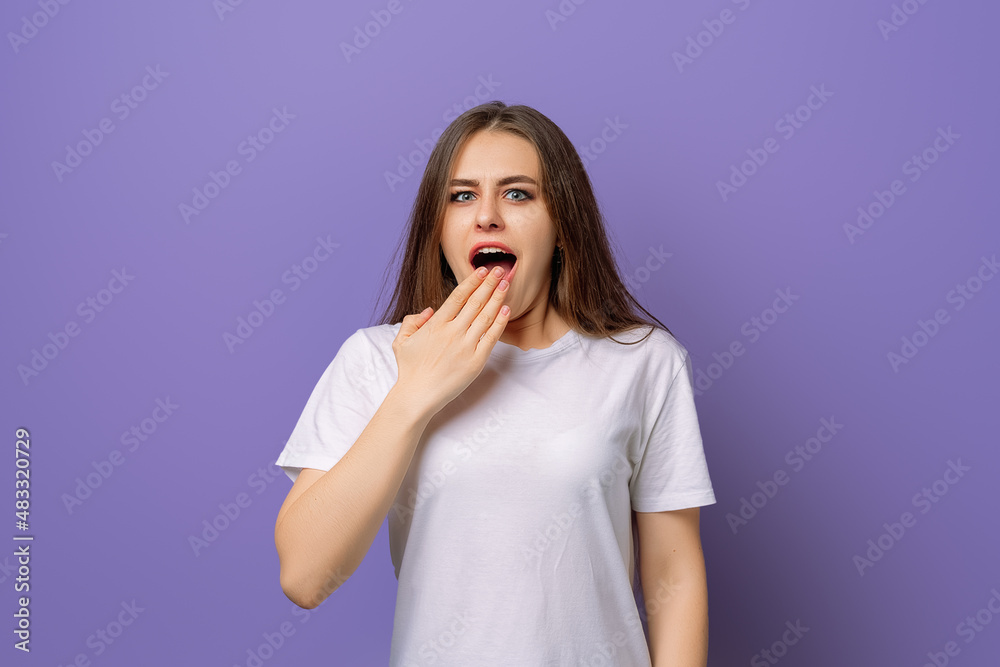 Surprised girl covers her mouth with her hand, hear amazing news, standing in blank white t shirt over purple background Surprised girl covers her mouth with her hand, hear amazing news, standing in blank white t shirt over purple background