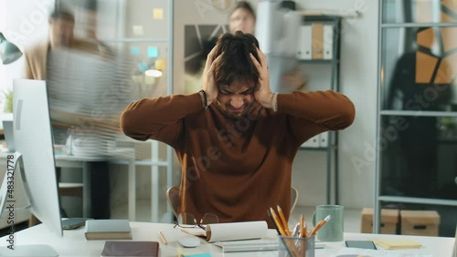 Time lapse zoom out shot of annoyed businessman covering his ears with hands while sitting at desk and suffering from loud noise in open office during workday photo