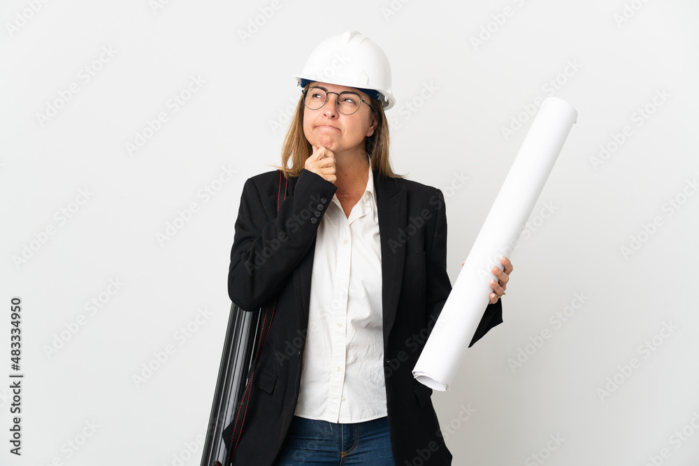 Middle age architect woman with helmet and holding blueprints over isolated background having doubts and thinking Middle age architect woman with helmet and holding blueprints over isolated background having doubts and thinking