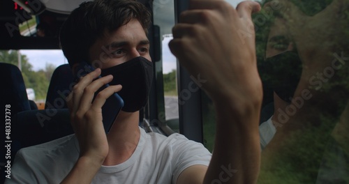 A man talking on the phone in a public transport bus. There is a mask on the face. He gives a verbal message to the interlocutor using telephony. Overcast.