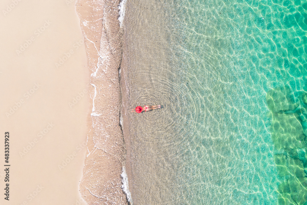 Top view. Young beautiful woman in a red hat and bikini lying and sunbathe in sea water on the sand beach. Drone, copter photo. Summer vacation. View from above.