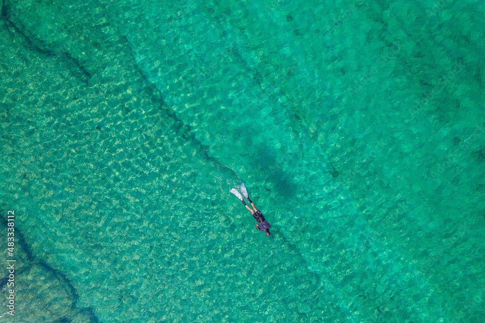 Spearfishing scuba diver in tropical exotic sea, ocean turquoise clear water. Man swimming hunting exotic fish, poaching. Top view. Aerial, drone, copter view.