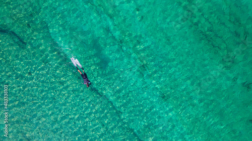 Spearfishing scuba diver in tropical exotic sea, ocean turquoise clear water. Man swimming hunting exotic fish, poaching. Top view. Aerial, drone, copter view. © flowertiare