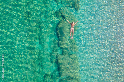 Top view. Young beautiful naked woman in a hat swimming in sea water on sand beach. Drone  copter photo. Summer vacation. View from above.