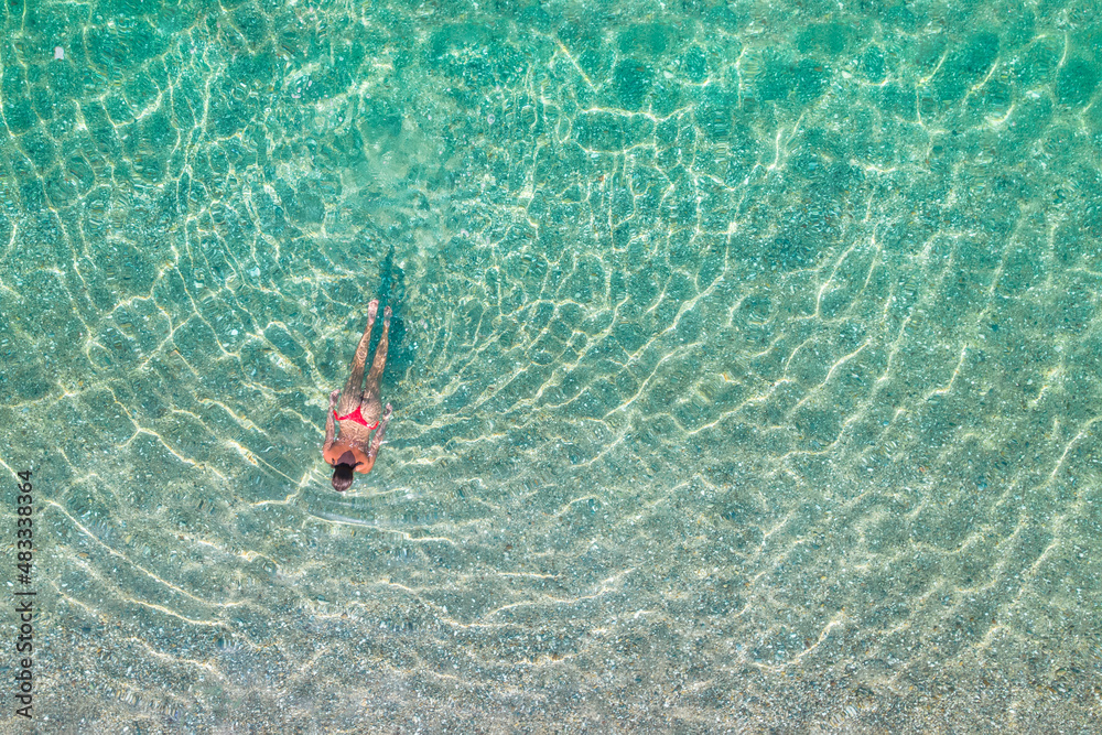 Top, aerial view. Young beautiful woman in a red bikini panties swimming in sea water on the sand beach. Drone, copter photo. Summer vacation. View from above.