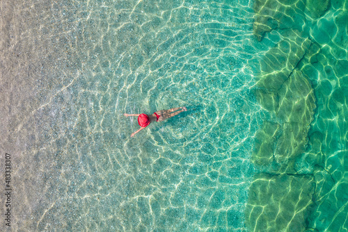 Top view. Young beautiful woman in a red hat and bikini swimming in sea water on the sand beach. Drone, copter photo. Summer vacation. View from above.