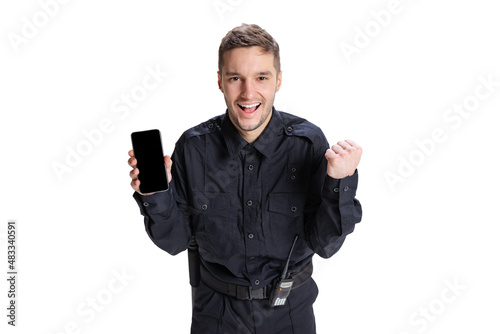 Portrait of young man, policeman officer wearing black uniform using phone isolated on white background. Concept of job, caree, law and order. photo