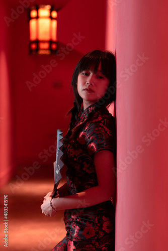 A chinese girl is standing against a red wall in a Chinese dress qipao on a chinese designed place