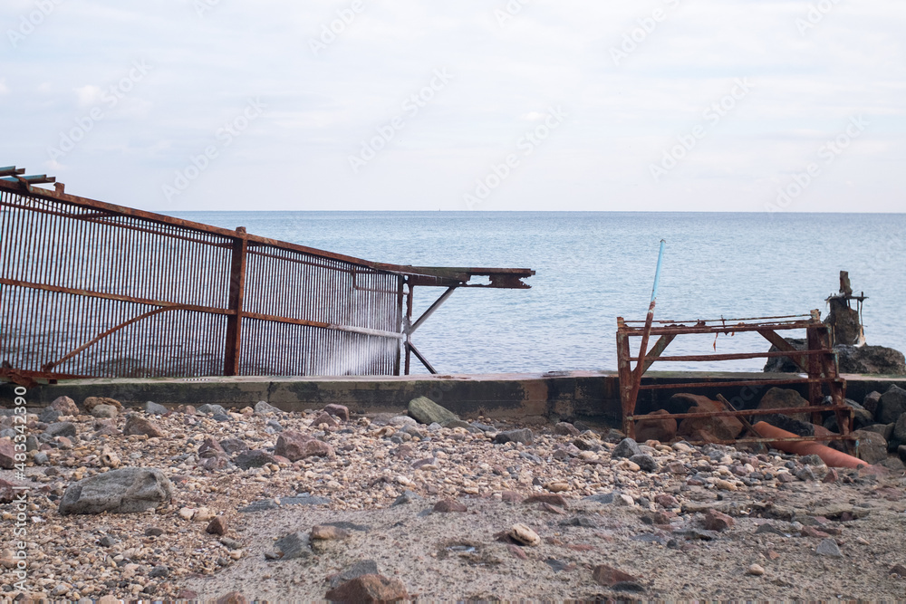 destroyed with a sea storm rusty metal pier. metal steps lead in the sea destroyed with a sea storm rusty metal pier. metal steps lead in the sea