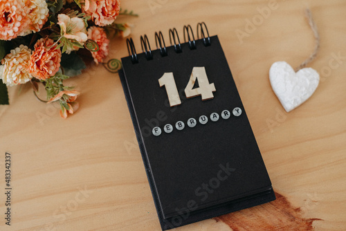 Wooden calendar on February 14 with roses and heart.