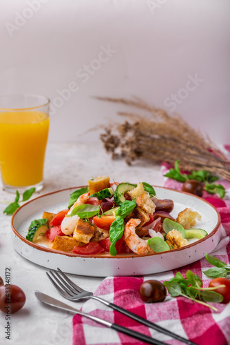 Panzanella with shrimp, tomatoes, cucumber, avocado, croutons and basil. Traditional healthy Italian salad with tomatoes and bread. Fresh italian summer salad with a glass of orange juice.