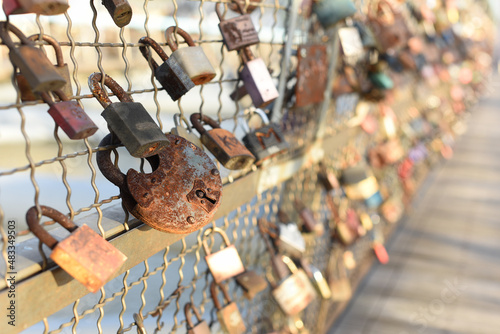 Old rusty love lock hanging on a bridge on the blurry background of other locks. Valentine's Day and Love concept.
