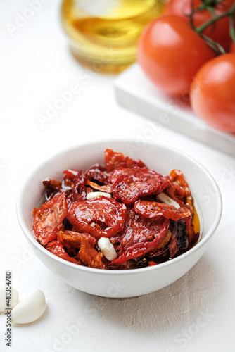 Sun dried tomatoes  on white bowl, white wooden background. Dried tomatoes with olive oil, salt, herbs and garlic recipe.  Top view,  copyspace.