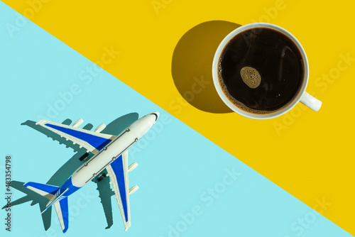 Decorative passenger plane and cup of coffee on blue and yellow background. Holiday concept.