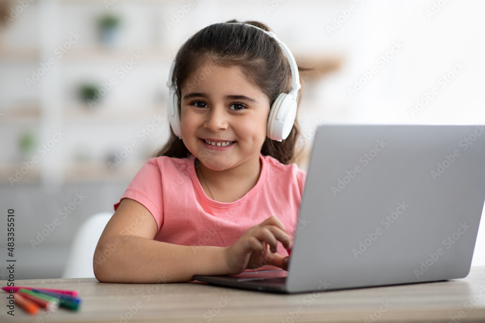 Cute Little Arab Girl Wearing Wireless Headphones Using Laptop At Home Cute Little Arab Girl Wearing Wireless Headphones Using Laptop At Home